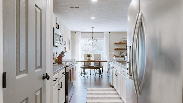 kitchen with visible vents, light wood-style flooring, stainless steel appliances, a textured ceiling, and white cabinetry