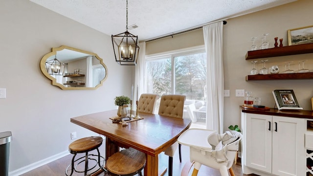 dining space featuring visible vents, a textured ceiling, wood finished floors, an inviting chandelier, and baseboards