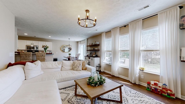 living room with an inviting chandelier, baseboards, visible vents, and a textured ceiling