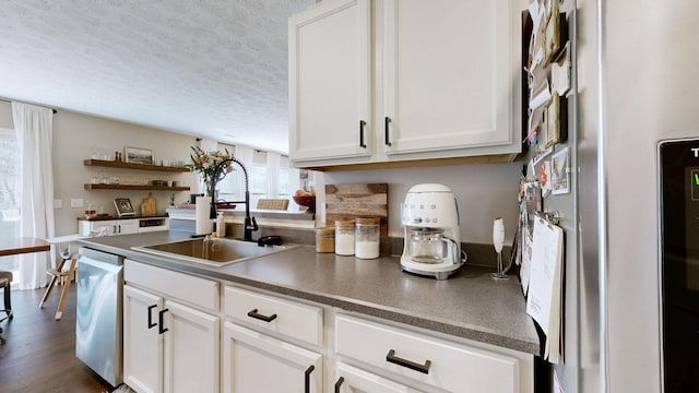 kitchen featuring dark countertops, appliances with stainless steel finishes, white cabinets, a textured ceiling, and a sink