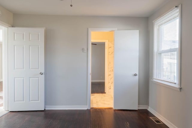 unfurnished bedroom featuring visible vents, connected bathroom, baseboards, and wood finished floors