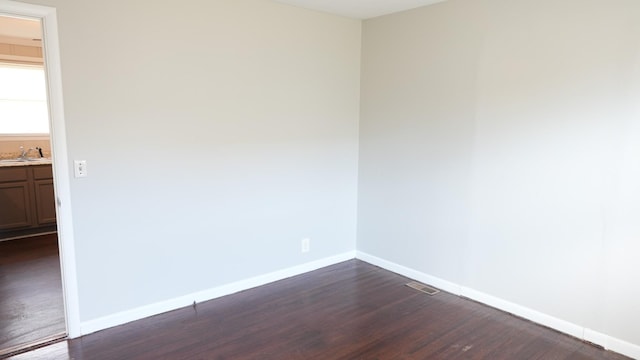 spare room with a sink, visible vents, baseboards, and dark wood-style floors