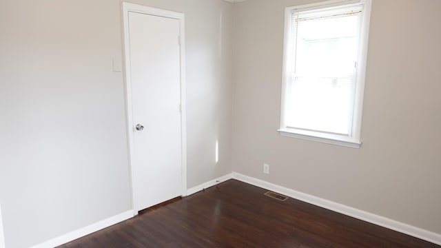 empty room with dark wood finished floors, visible vents, and baseboards