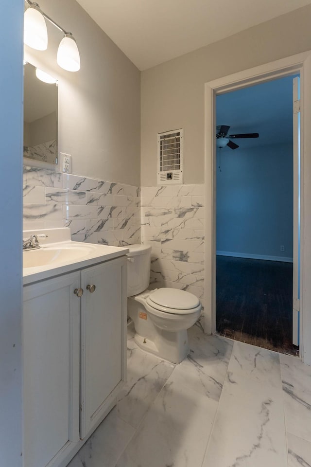 bathroom featuring vanity, heating unit, tile walls, toilet, and marble finish floor