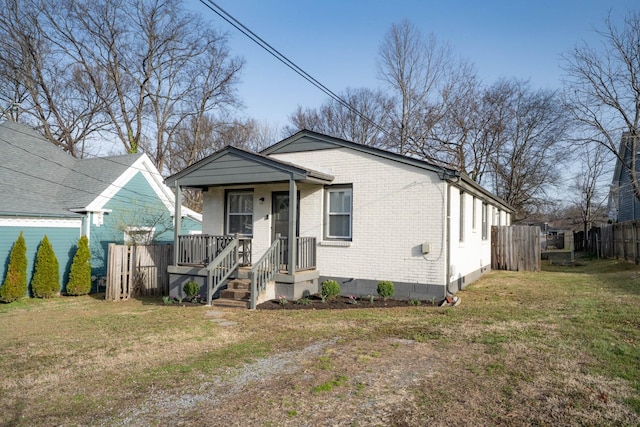 view of front of house featuring brick siding, covered porch, a front yard, and fence