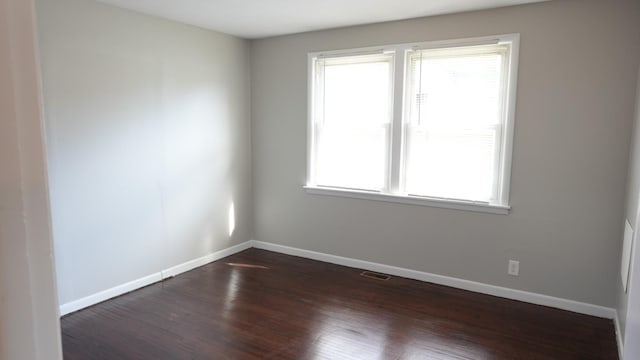 unfurnished room with dark wood-type flooring, visible vents, and baseboards