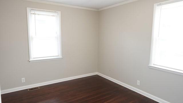 spare room with a wealth of natural light, visible vents, baseboards, and dark wood-style flooring