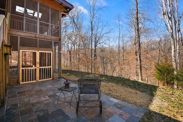 view of patio featuring a forest view, french doors, and a sunroom