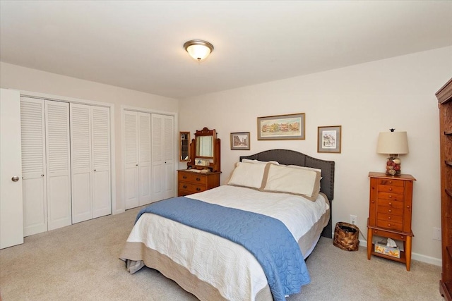 bedroom featuring light carpet and two closets