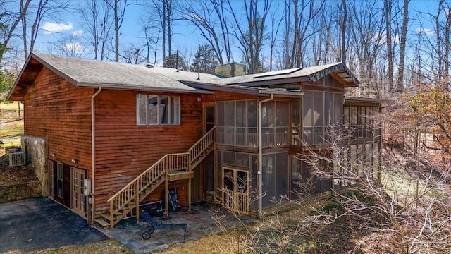 back of house featuring a chimney, a sunroom, stairway, cooling unit, and a patio