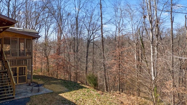view of yard featuring stairway, a view of trees, a patio area, and a sunroom