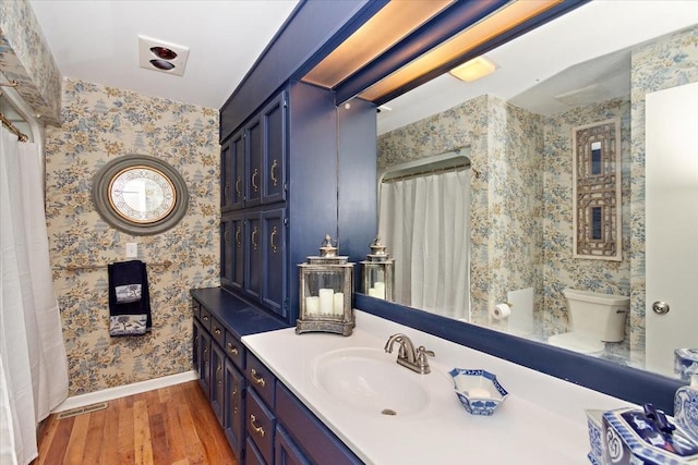 full bath featuring vanity, visible vents, wood finished floors, baseboards, and wallpapered walls