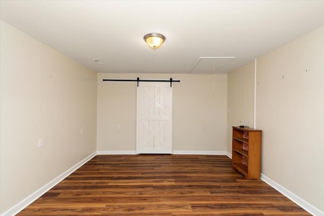empty room featuring baseboards, attic access, wood finished floors, and a barn door
