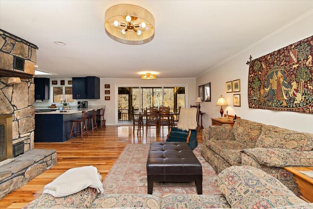 living area featuring light wood-style floors, ornamental molding, a stone fireplace, and a chandelier