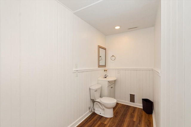 half bathroom featuring visible vents, wainscoting, wood finished floors, toilet, and a sink