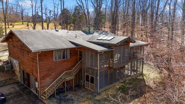 rear view of property featuring a shingled roof, a sunroom, stairway, a chimney, and cooling unit