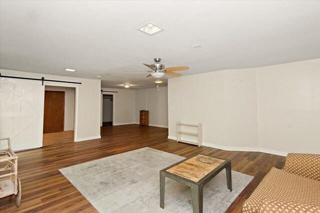unfurnished living room featuring baseboards, ceiling fan, a barn door, and wood finished floors