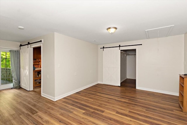 unfurnished bedroom featuring attic access, a barn door, wood finished floors, baseboards, and access to outside
