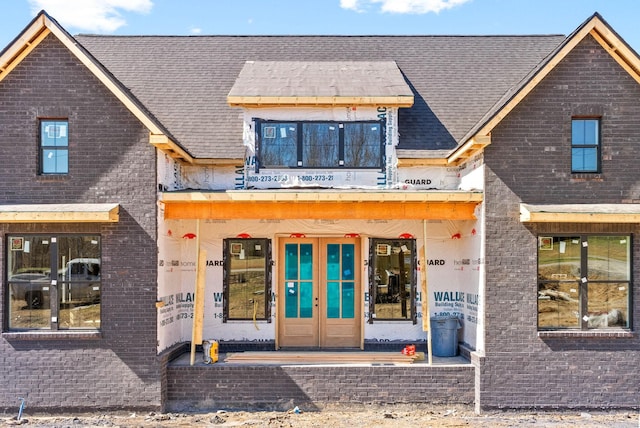 view of front of house featuring brick siding, french doors, and roof with shingles