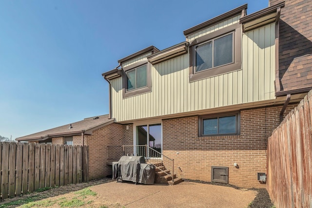 back of property featuring brick siding, a shingled roof, and fence