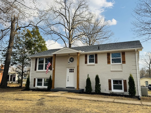 raised ranch featuring brick siding, central air condition unit, and roof with shingles