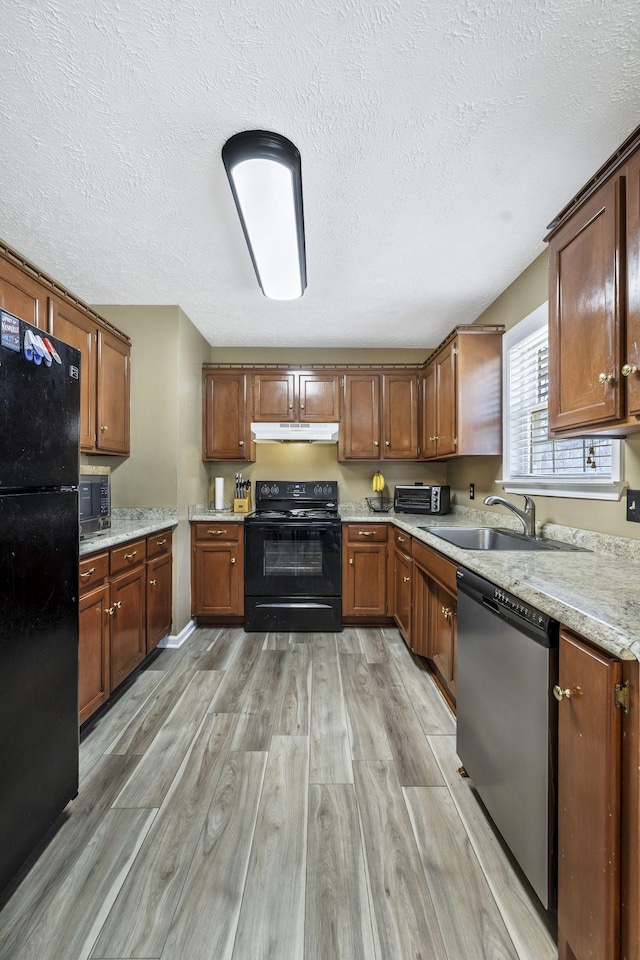 kitchen featuring black appliances, under cabinet range hood, a sink, light wood-style floors, and brown cabinetry