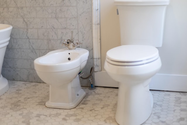 bathroom with a bidet, toilet, and tile walls