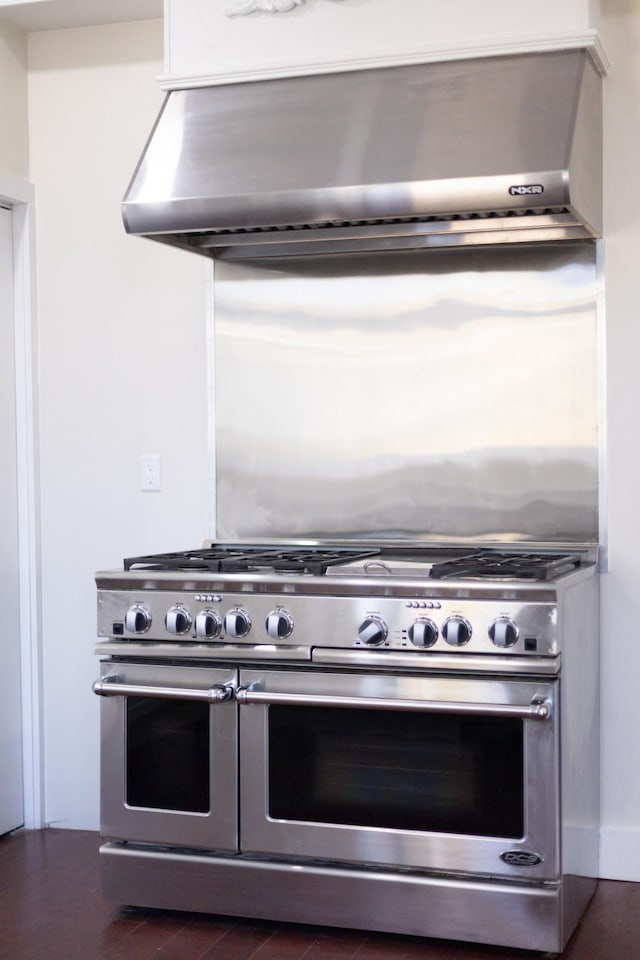 kitchen featuring double oven range, wall chimney exhaust hood, and wood finished floors