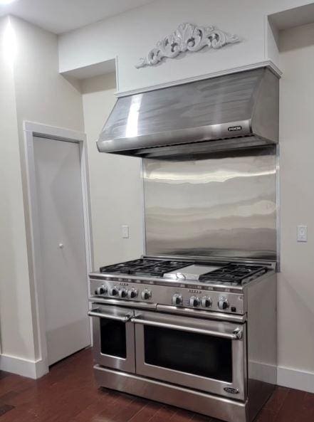 kitchen featuring range with two ovens, baseboards, dark wood-type flooring, and wall chimney range hood