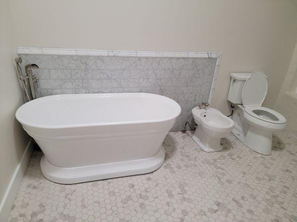 full bathroom featuring tile walls, toilet, a bidet, and a freestanding bath