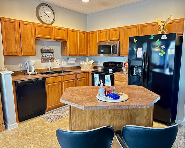 kitchen with black appliances, a center island, brown cabinetry, and a sink