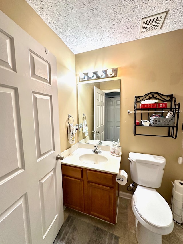 bathroom featuring visible vents, toilet, a textured ceiling, baseboards, and vanity