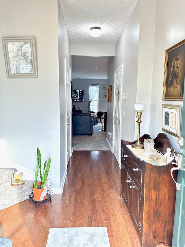 hall featuring a textured ceiling, baseboards, and wood finished floors