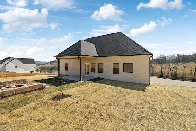 back of house featuring a yard, an outdoor fire pit, a shingled roof, and a patio area