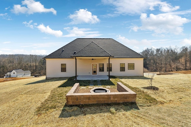 back of house with a patio, a ceiling fan, a forest view, roof with shingles, and a yard