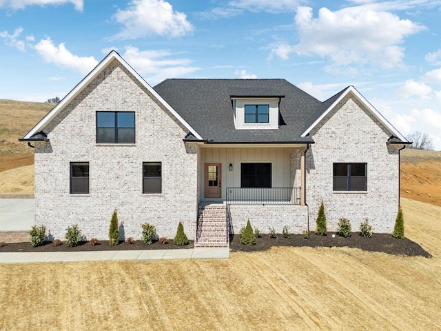 modern farmhouse style home featuring brick siding, covered porch, board and batten siding, and a front lawn