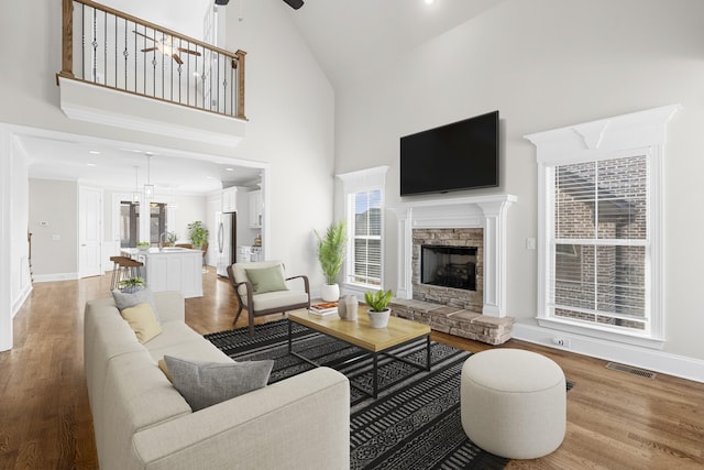 living room with a stone fireplace, light wood-style flooring, high vaulted ceiling, and baseboards