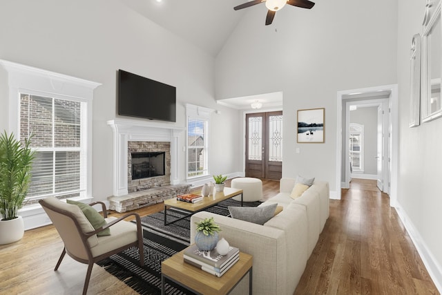 living area with baseboards, light wood finished floors, high vaulted ceiling, a fireplace, and french doors