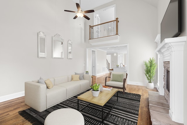 living room with light wood-style flooring, a ceiling fan, a high ceiling, a fireplace, and baseboards