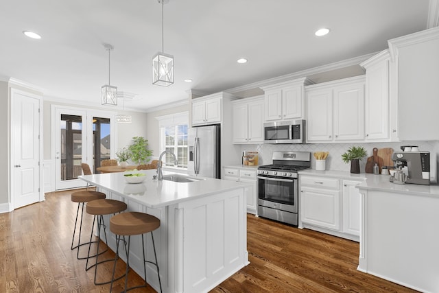 kitchen with dark wood-type flooring, a center island with sink, ornamental molding, a sink, and appliances with stainless steel finishes