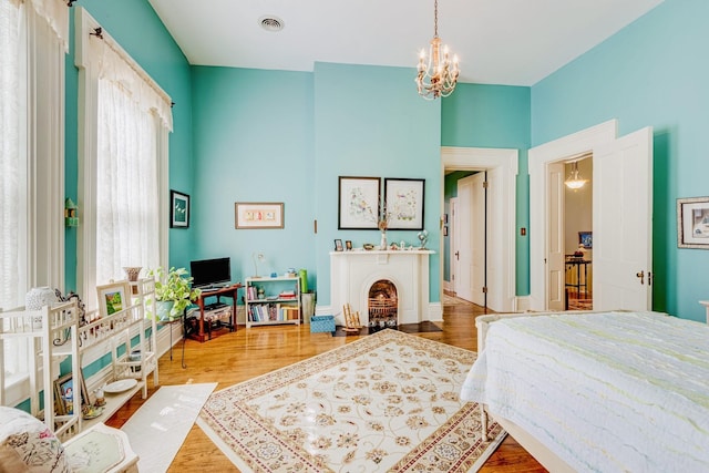 bedroom featuring wood finished floors, visible vents, baseboards, an inviting chandelier, and a fireplace