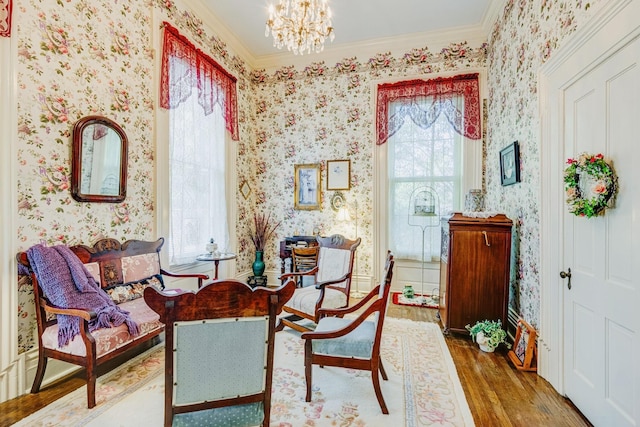 sitting room with a notable chandelier, wood finished floors, ornamental molding, and wallpapered walls