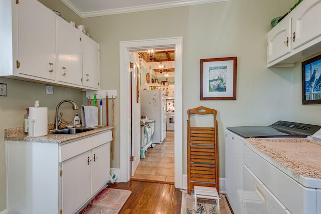 kitchen with a sink, wood finished floors, washing machine and dryer, white cabinets, and crown molding