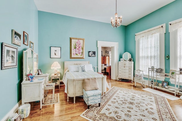 bedroom with a chandelier, ensuite bathroom, baseboards, and wood finished floors