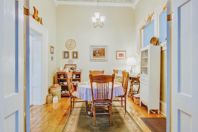 dining room with light wood finished floors, a notable chandelier, a towering ceiling, and ornamental molding