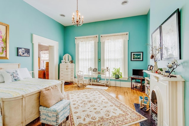 bedroom with visible vents, ensuite bathroom, an inviting chandelier, and wood finished floors