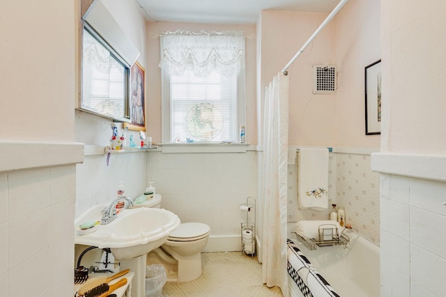 bathroom with a wainscoted wall, toilet, a tub to relax in, a shower with curtain, and tile walls