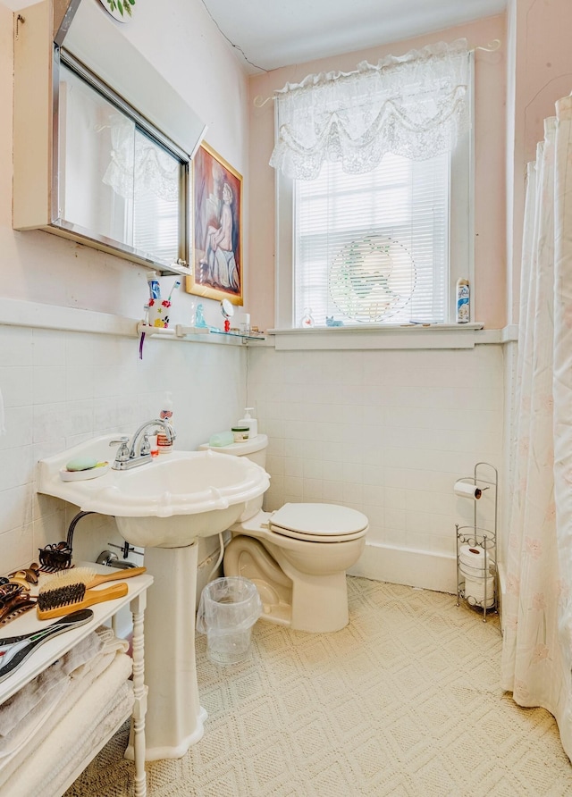 bathroom featuring a wainscoted wall, toilet, and tile walls