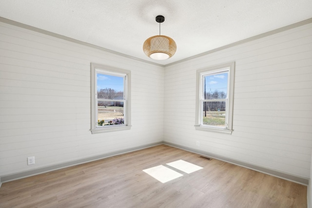 empty room with visible vents, plenty of natural light, baseboards, and wood finished floors