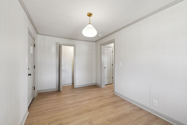 unfurnished bedroom featuring light wood finished floors, a textured ceiling, baseboards, and ornamental molding